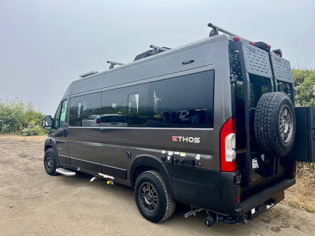 Dark grey Ethos overland camper van, equipped for off-road rv rental. Features roof rack & rear gear carrier.