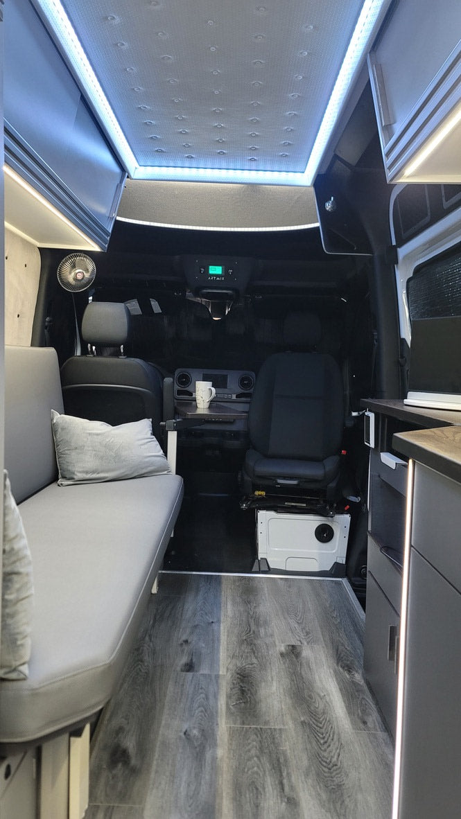 RV rental: Camper van interior with comfy bench, wood floor, bright LED lighting, and driver's cabin view for travel.