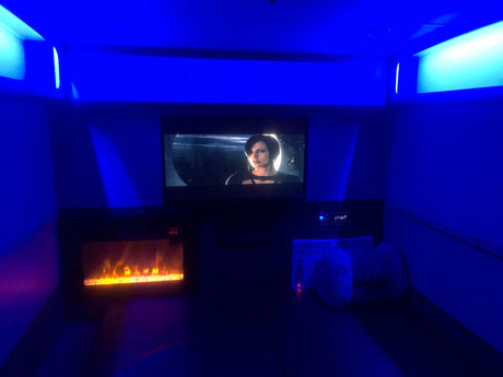 RV rental's cozy interior: blue lighting, TV with a movie, and an electric fireplace creating a relaxing atmosphere.