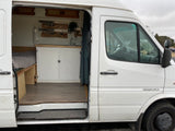 White Sprinter camper van for RV rental, showing interior kitchenette, bed, and driver's area.