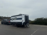 White & black Cherokee Wolf Pup RV rental and pickup truck parked by the ocean on a cloudy day.