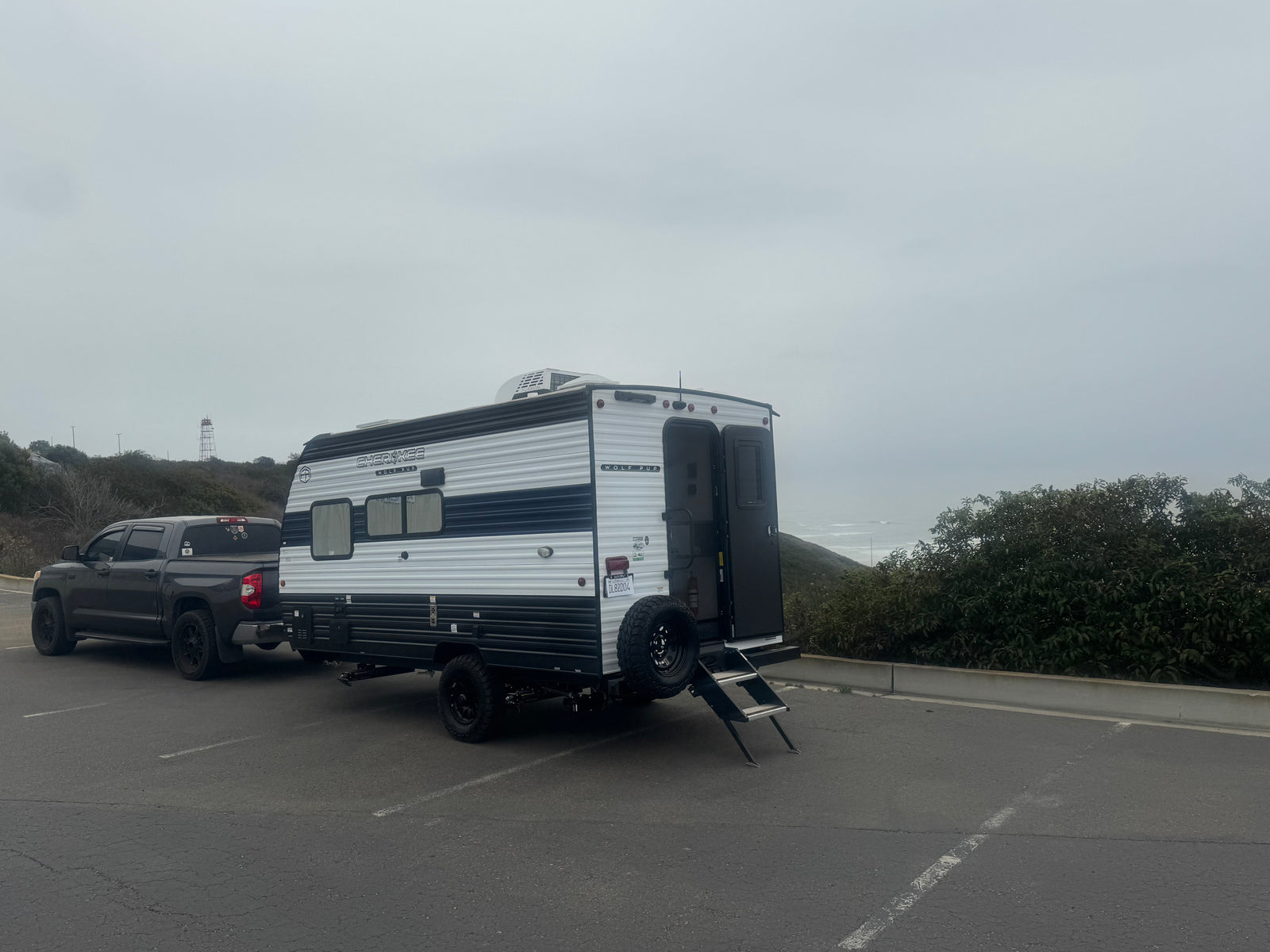 White & black Cherokee Wolf Pup RV rental and pickup truck parked by the ocean on a cloudy day.