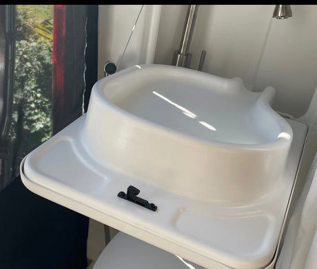 Inside an RV rental: a compact white sink/toilet unit with a faucet, ideal for maximizing space on the road.