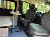Cozy RV rental interior with swiveling seats, a small table, mugs, and a scenic forest view from the window.