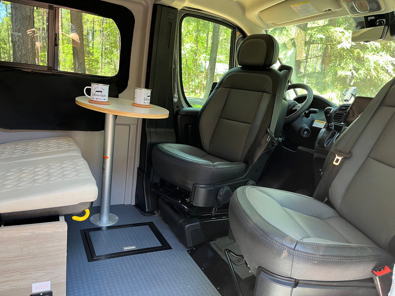 Cozy RV rental interior with swiveling seats, a small table, mugs, and a scenic forest view from the window. — photo 7