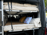 Rear view of an RV rental's interior, showing a modular dual-level bunk bed system with bedding for a comfortable stay.