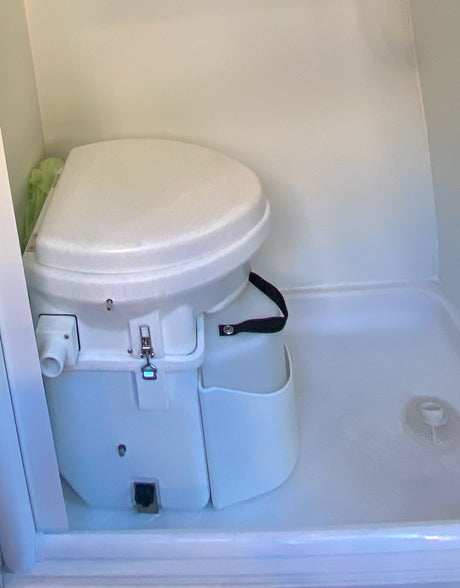 A white composting toilet in an RV rental bathroom, integrated into a shower stall. Ideal for off-grid living.