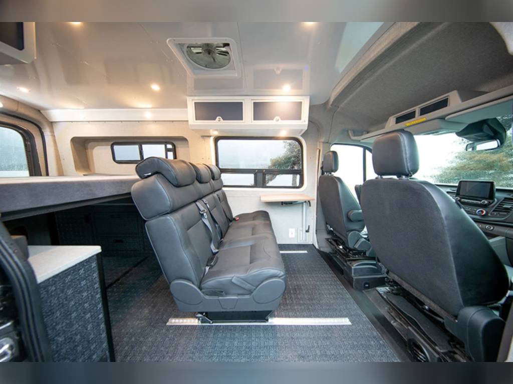 Spacious RV rental interior featuring a long bench seat, overhead storage, and a raised bed area for comfortable travel.