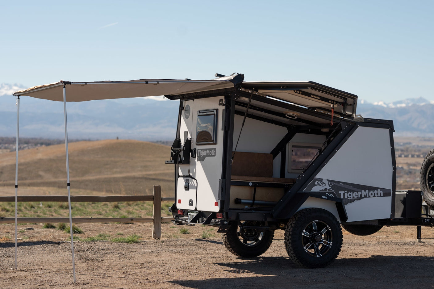 An off-road TigerMoth **RV rental** trailer, with its awning extended, offers adventure in a mountain setting.