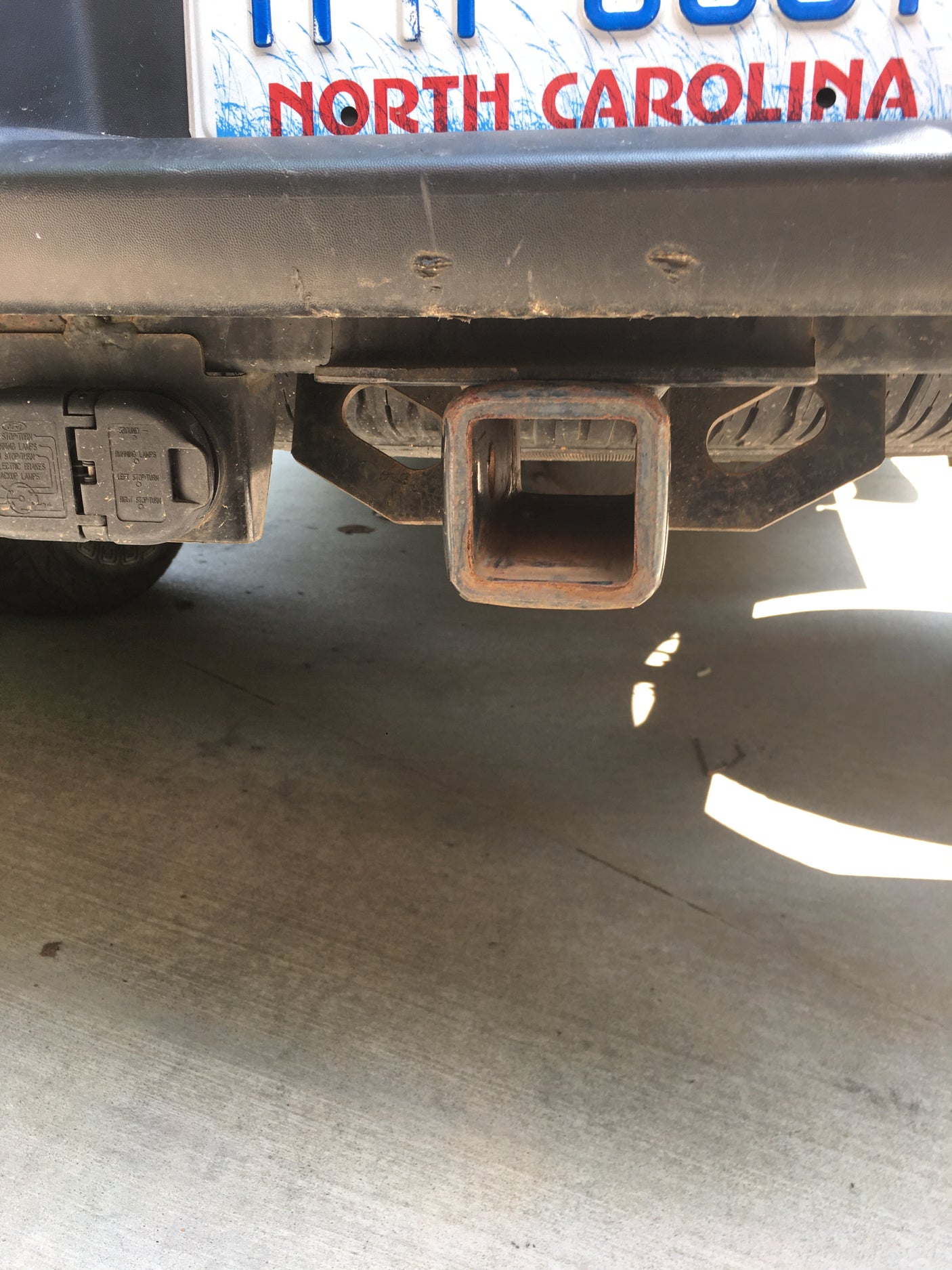 Rear of an RV rental or vehicle, showing its North Carolina license plate, trailer hitch receiver, and electrical connector for towing.