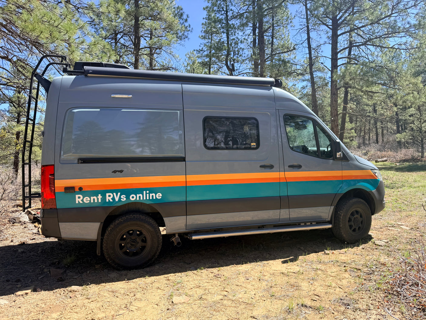 Gray rv rental camper van with orange & teal stripes parked in a sunny pine forest, ready for adventure.