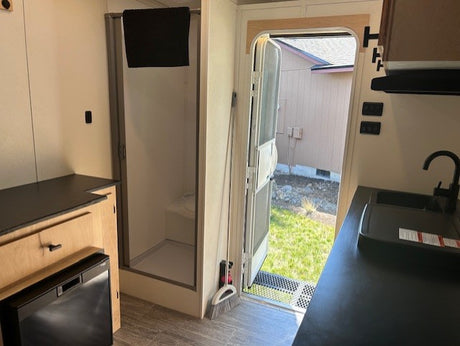 This rv rental features a compact kitchen (sink, fridge), walk-in shower, and an open door. Designed for functional, mobile living.
