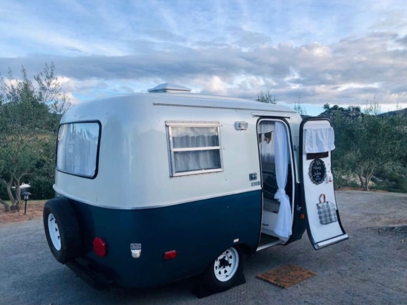  playing cards outside their charming vintage RV rental with an extended awning.|Explore in style! This charming two-toned vintage compact RV rental offers cozy travel and outdoor stays.|Stylish RV rental interior: compact kitchen with stove — photo 2