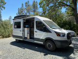 Adventure awaits! This white Ford Transit camper van, an excellent RV rental choice, is parked on a sunny gravel lot, side door open.