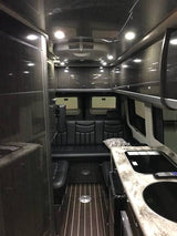 Inside a luxurious **RV rental**, showing a modern kitchenette, plush black seating, and sleek dark wood interior.