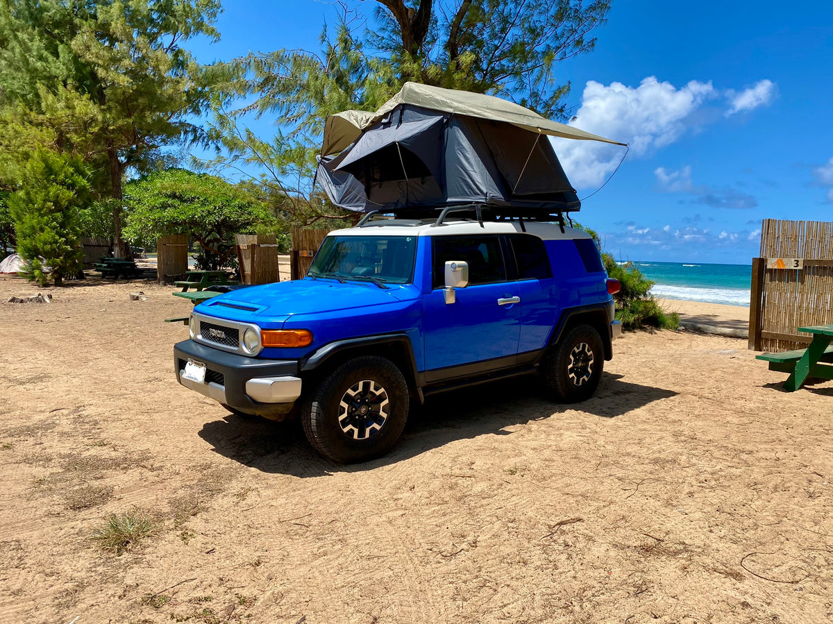Blue FJ Cruiser with rooftop tent, ready for a beach camping RV rental adventure, parked on sand by the ocean. — photo 9
