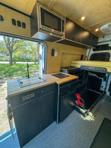 Spacious RV rental van interior: custom kitchen with sink, cooktop, microwave, smart storage, and comfortable sleeping area. Ready for adventure!