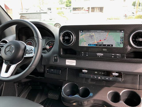View of a modern Mercedes RV rental interior dashboard, featuring a navigation screen, steering wheel, and climate controls.