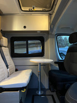 Inside a cozy **rv rental**: quilted bench seat, round table, and front passenger seat. Ideal for your next adventure.