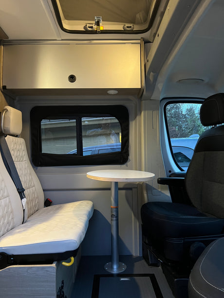 Inside a cozy **rv rental**: quilted bench seat, round table, and front passenger seat. Ideal for your next adventure.