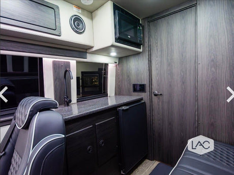 Modern RV rental interior: a compact kitchenette with sink, microwave, fridge, and passenger seating area.