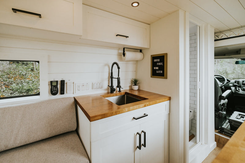 Experience compact comfort in this modern RV rental's kitchen and living area, featuring a cozy bench and full amenities. — photo 7