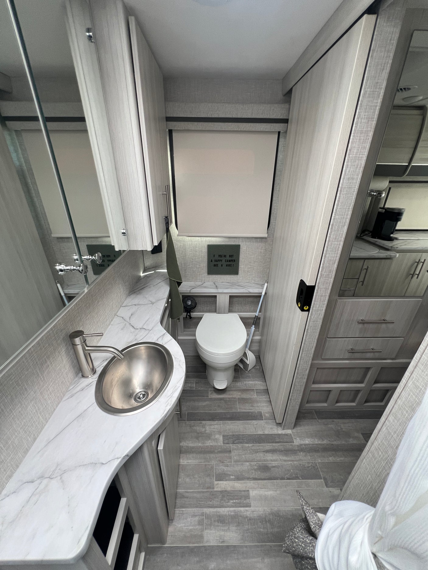 Bright, modern rv rental bathroom featuring a sink, toilet, and a playful 'Happy Camper' sign on the wall.