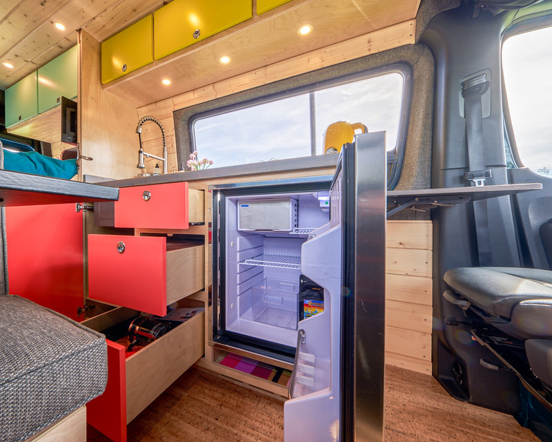 RV rental interior shows a bright kitchen with red & yellow cabinets, a stainless sink, and an open fridge. — photo 17