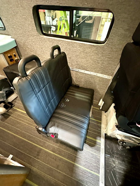 RV rental interior: A black bench seat with seatbelts sits on striped flooring.