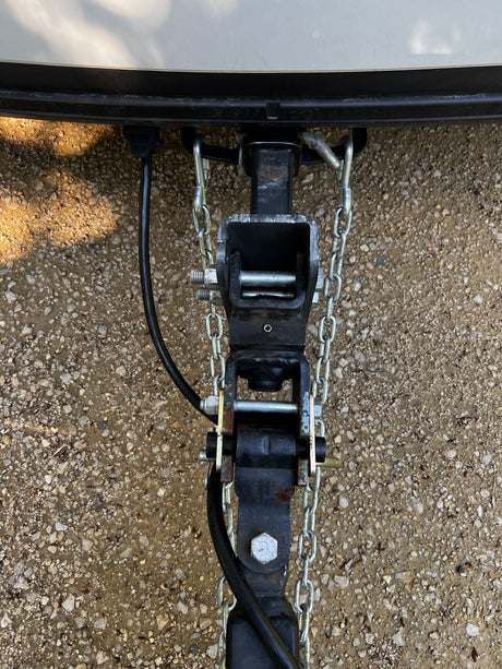 Close-up of an RV rental's weight distribution hitch and safety chains, providing secure trailer towing connection.