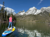 A woman paddleboards on a lake with stunning snow-capped mountains.