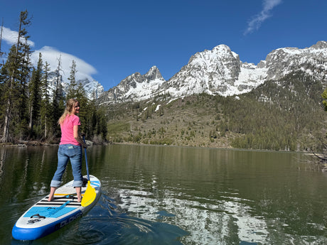 A woman paddleboards on a lake with stunning snow-capped mountains.