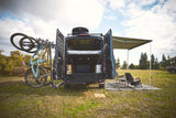 Kickstart your adventure! This RV rental camper van features bike mounts, a cozy interior, and a shaded outdoor camp setup.