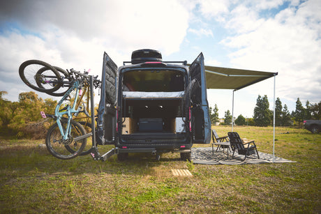 Kickstart your adventure! This RV rental camper van features bike mounts, a cozy interior, and a shaded outdoor camp setup.