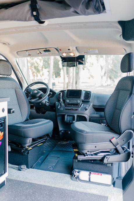 RV rental: Inside a modern camper van cockpit, showing driver/passenger seats, dashboard, and fire extinguisher.