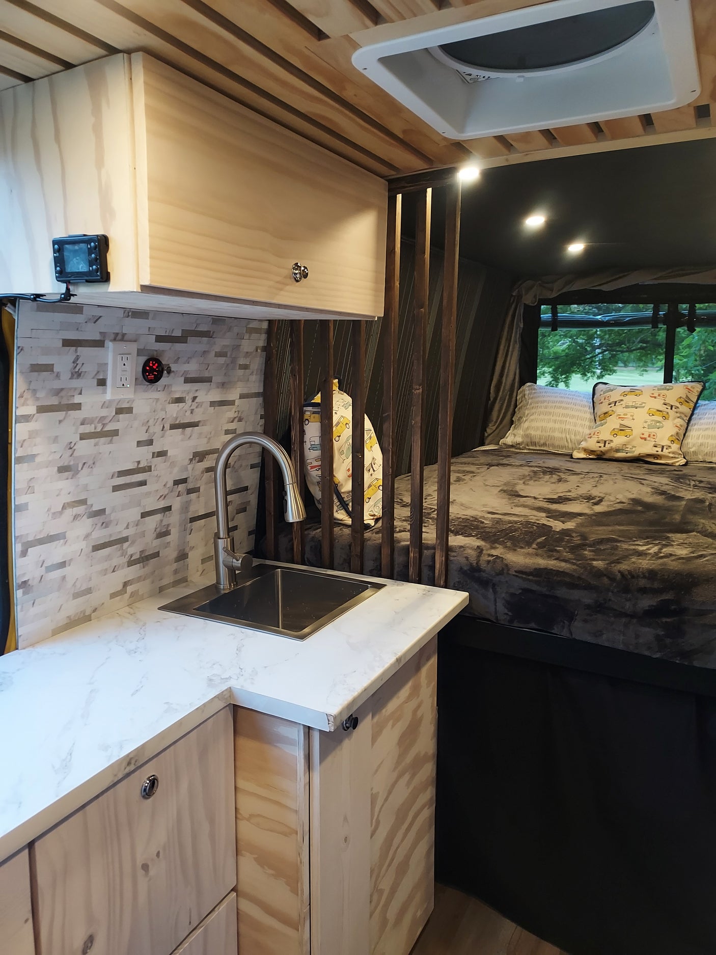 Cozy RV rental interior: wood-paneled walls, modern kitchen, comfortable bed, and scenic window.