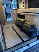 RV rental interior featuring a practical kitchenette, bed, and accessible floor storage area with bags.