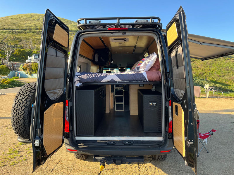 Explore this stylish RV rental camper van with open rear doors, revealing a comfy bed, storage, and custom wood interior. Adventure awaits! — photo 9