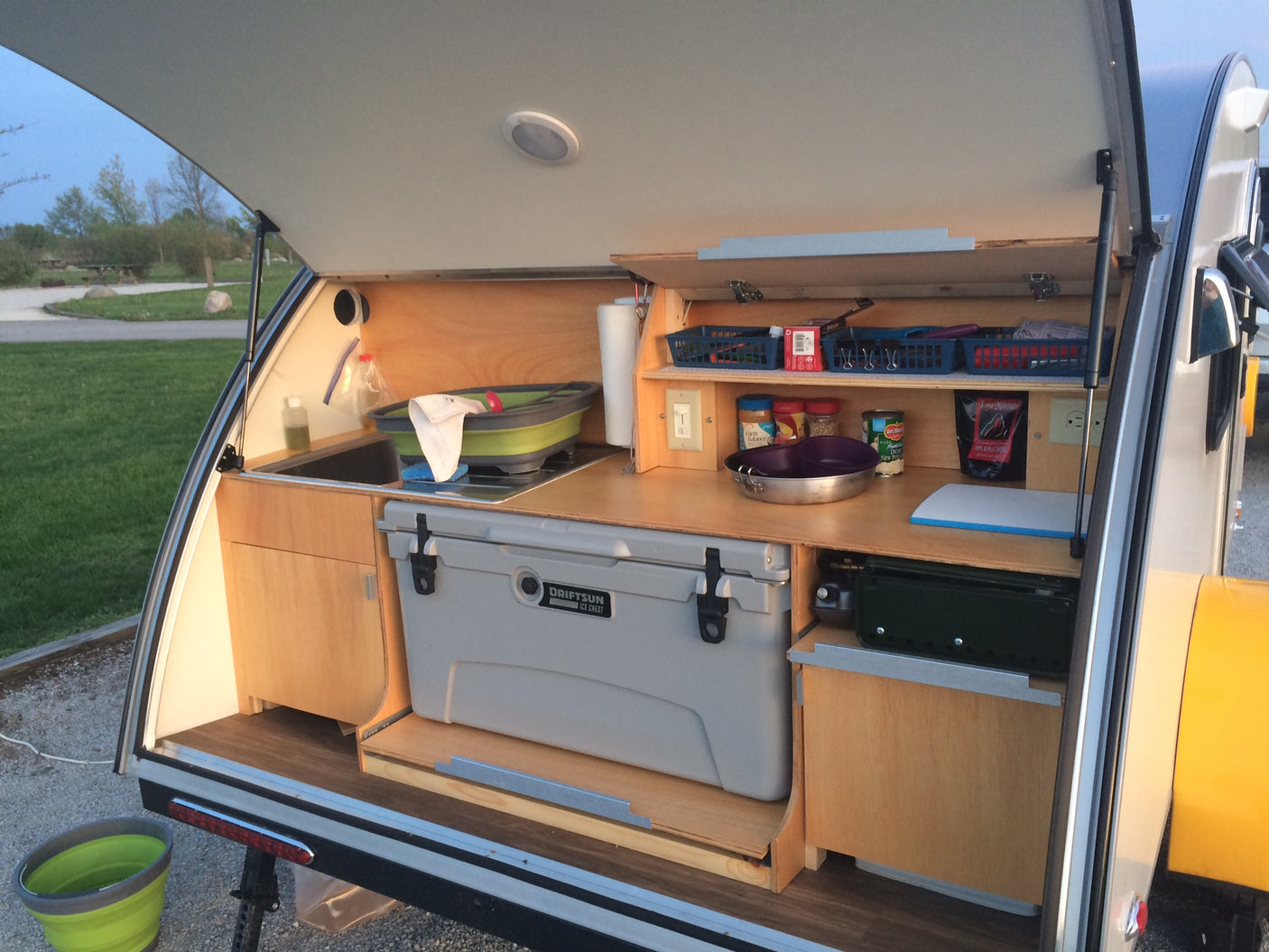 This compact rv rental outdoor kitchen boasts a sink, cooler, stove, and smart storage inside a teardrop camper.