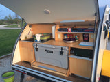 This compact rv rental outdoor kitchen boasts a sink, cooler, stove, and smart storage inside a teardrop camper.