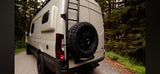 Modern campervan for rv rental, featuring a rear spare tire & ladder, parked by a forest road. Perfect for adventure.