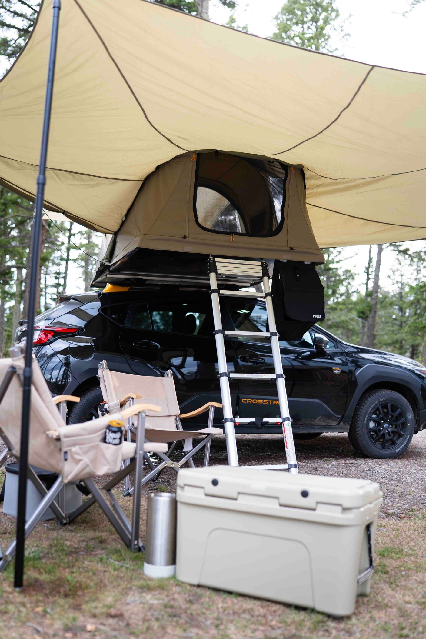 Car camping ready! This black Subaru Crosstrek with a rooftop tent, awning, chairs, and cooler offers a flexible RV rental alternative.