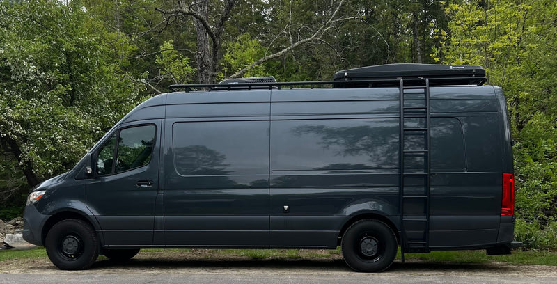 Explore with this dark gray Mercedes Sprinter RV rental. A custom camper van with roof rack & ladder, parked in nature. — photo 1