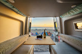 Perfect RV rental evening: beach sunset from inside a cozy camper van, with wine, cards, and ocean views.