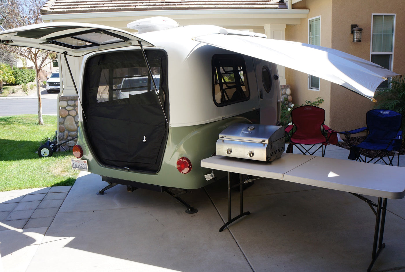 Teardrop RV rental, with rear hatch open to screen, side awning, portable grill on table, and chairs on driveway. — photo 6