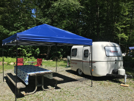 RV rental camping: A white Scamp travel trailer is set up at a shaded campsite with a blue canopy and picnic table.