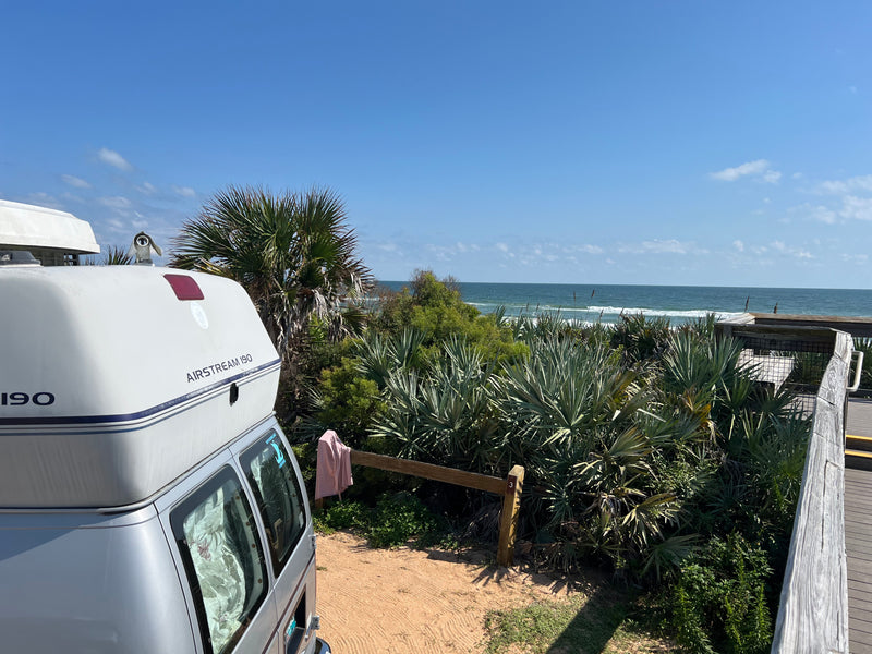 An Airstream 190 RV rental parked at a coastal campsite, offering views of the ocean waves beyond lush palm trees. — photo 13