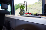 Modern rv rental kitchen with a sleek counter, sink, stovetop, and a vase of tulips, overlooking green hills.