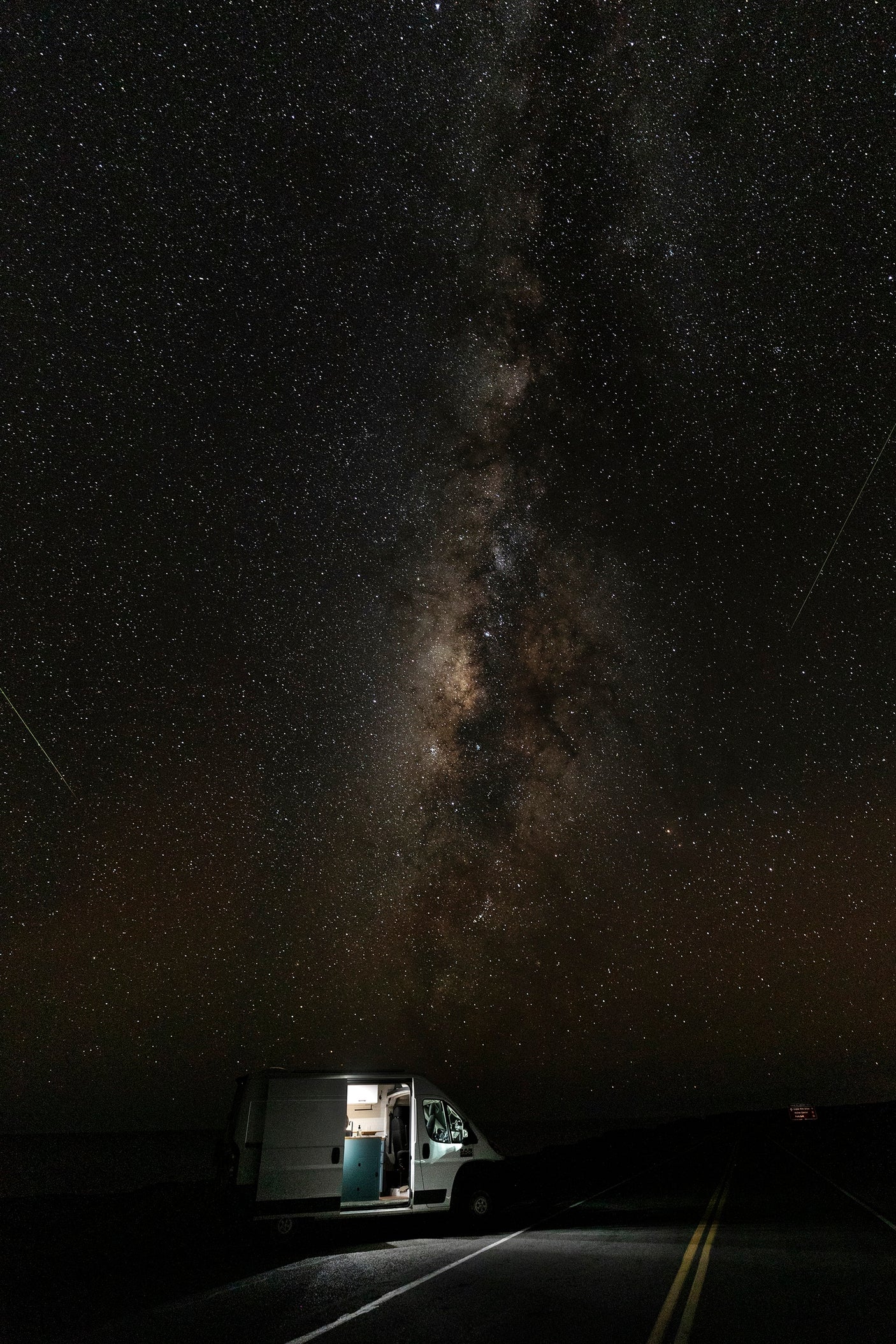 An RV rental illuminates a quiet road under a brilliant Milky Way, ideal for remote stargazing and van life adventures.
