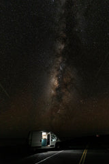 An RV rental illuminates a quiet road under a brilliant Milky Way, ideal for remote stargazing and van life adventures.